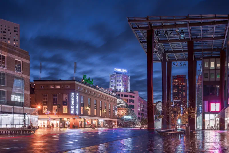 Wet city square (18 Septemberplein) at night with a covered walkway and the Philips tower (Lichttoren) beyond