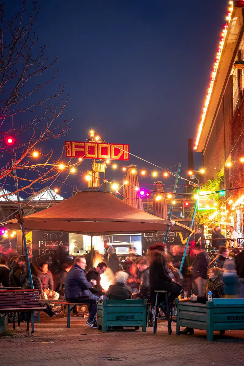 Crowd gathered around lights and a food stall at an evening street market (Strijp-S)