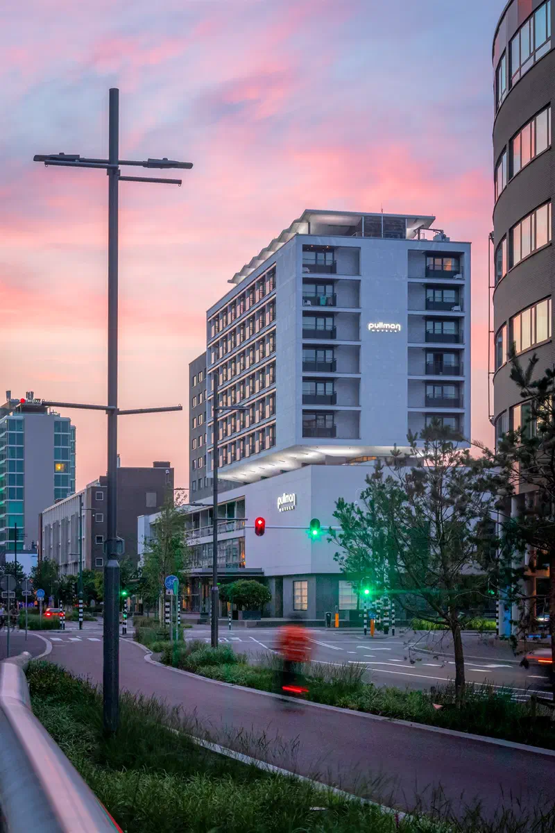 Modern hotel building (Pullman Eindhoven Cocagne) beside a cycle path under a pink evening sky