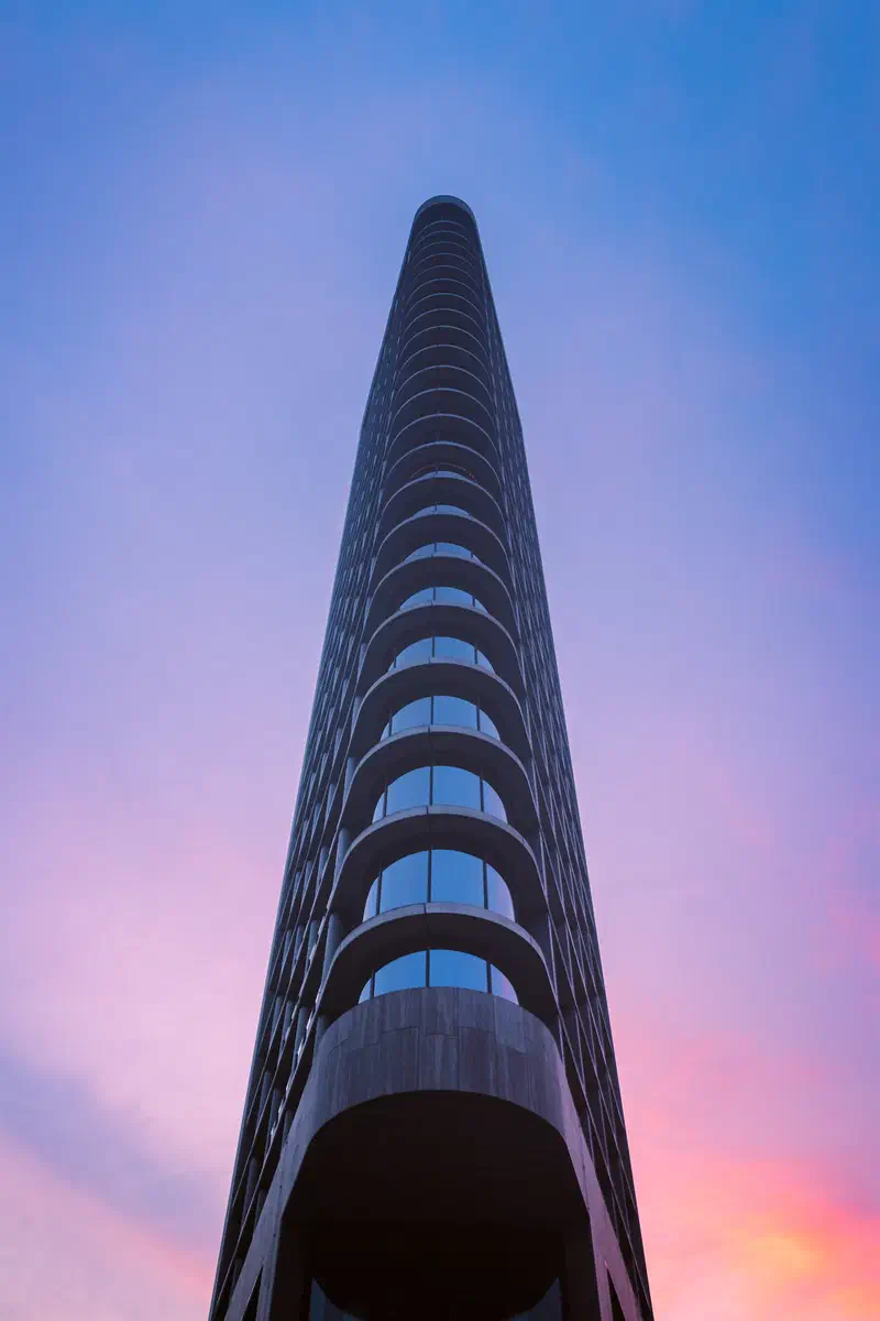 Looking up the curved facade of a slim tower (Vestedatoren) against a pink and purple sky