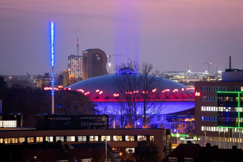 Purple-lit dome (Evoluon) building and a glowing blue mast across the city at dusk