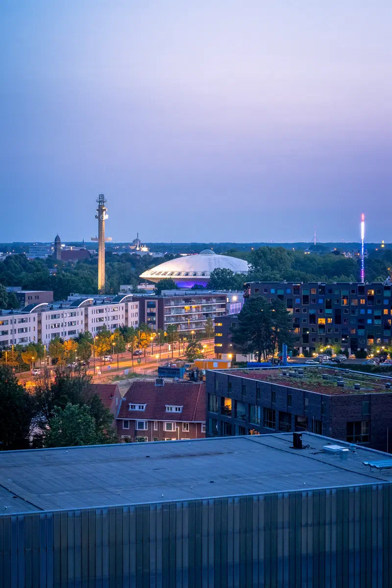 Domed building (Evoluon) and tall mast glowing above the city at dusk