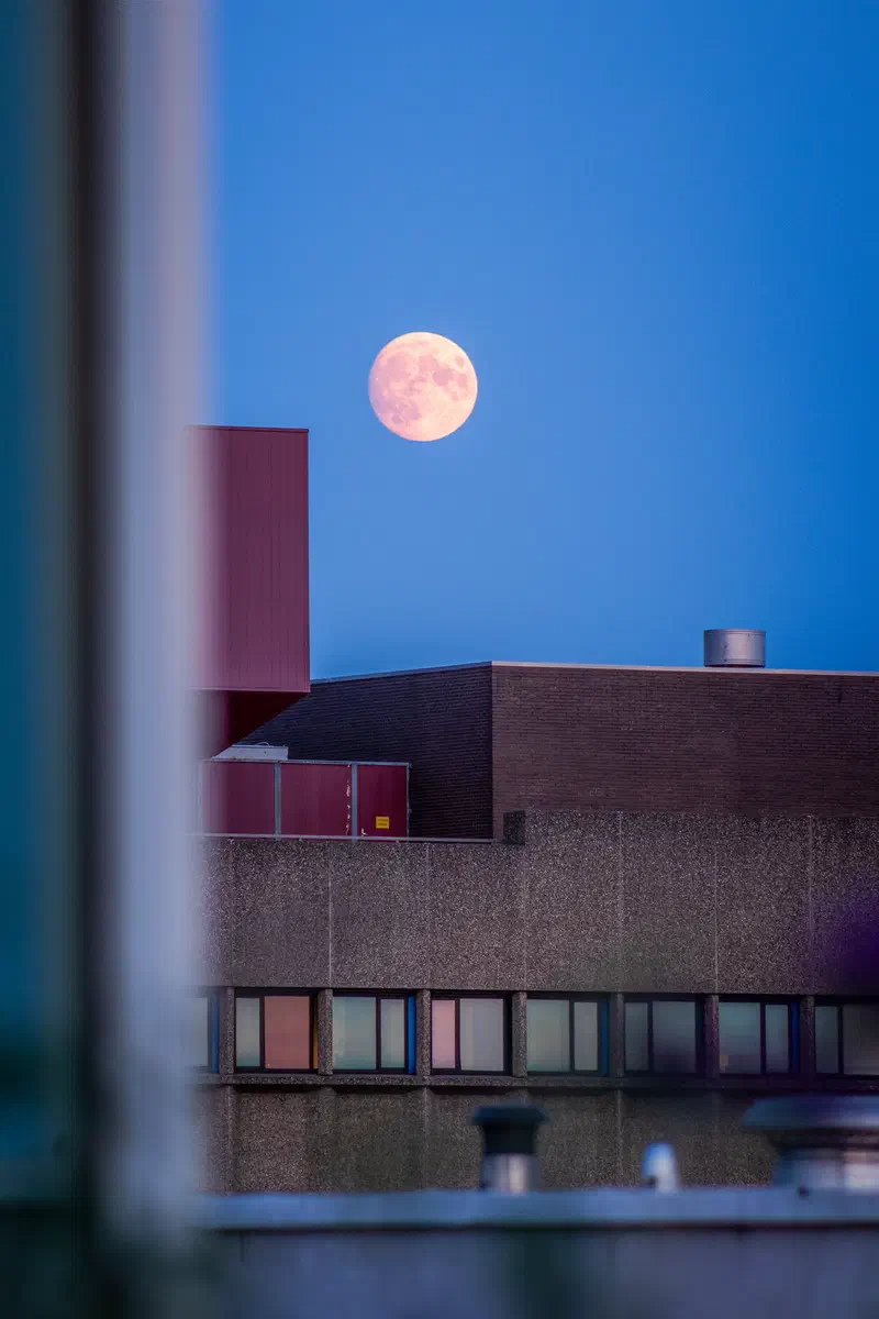 Full moon rising over a brick building (Strijp-S) seen past a window frame