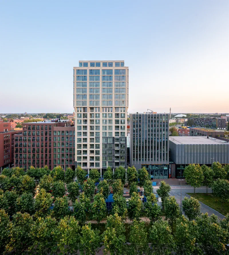 Modern residential towers (Strijp-S) behind a grove of young trees in evening light