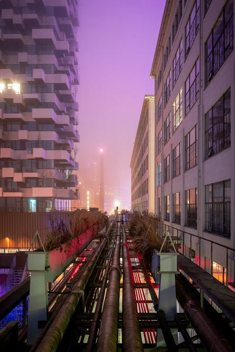 Pipes running between buildings (Trudo Toren & Hoge Rug) in pink and purple mist at dusk