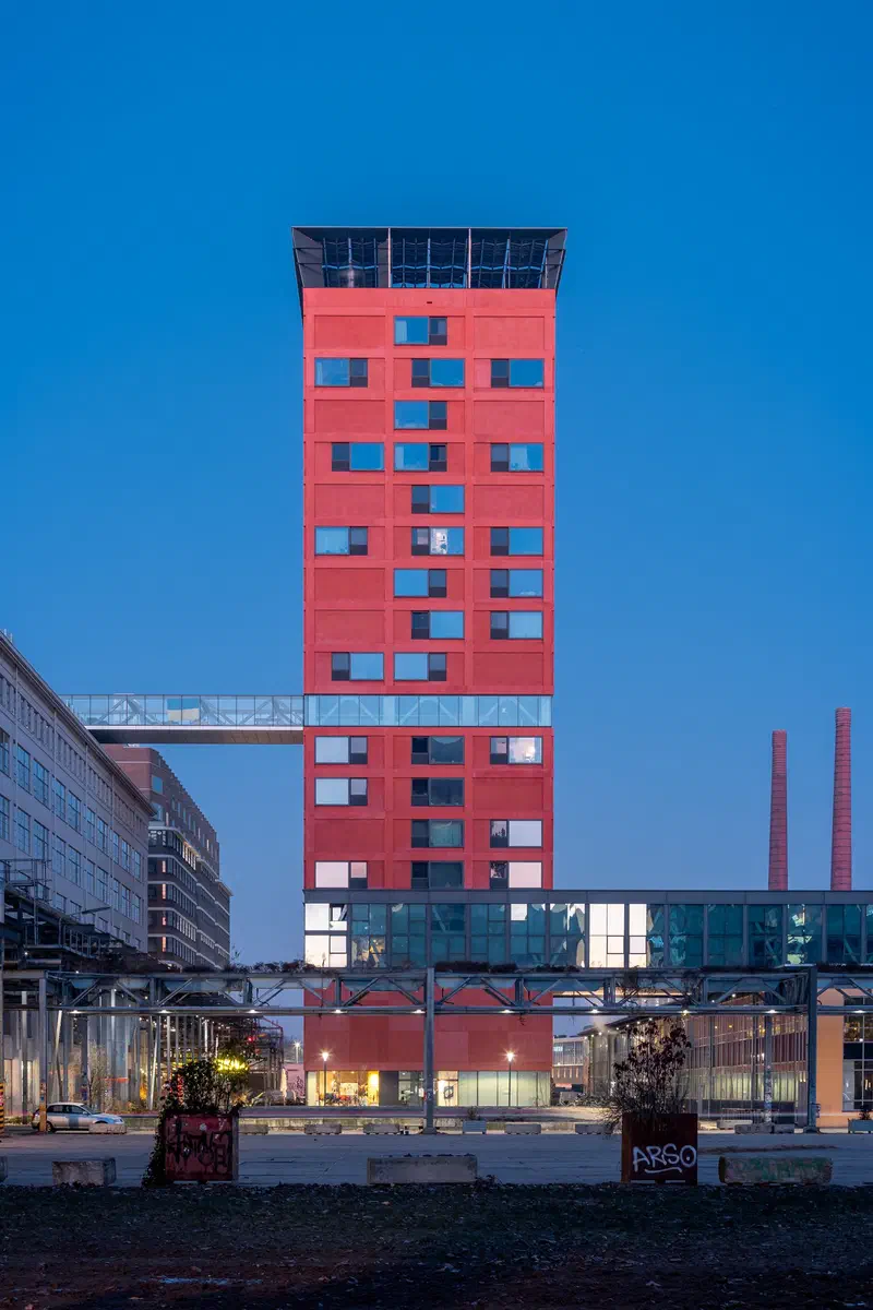 Red tower block (Haasje Over) with a glass bridge under a deep blue sky