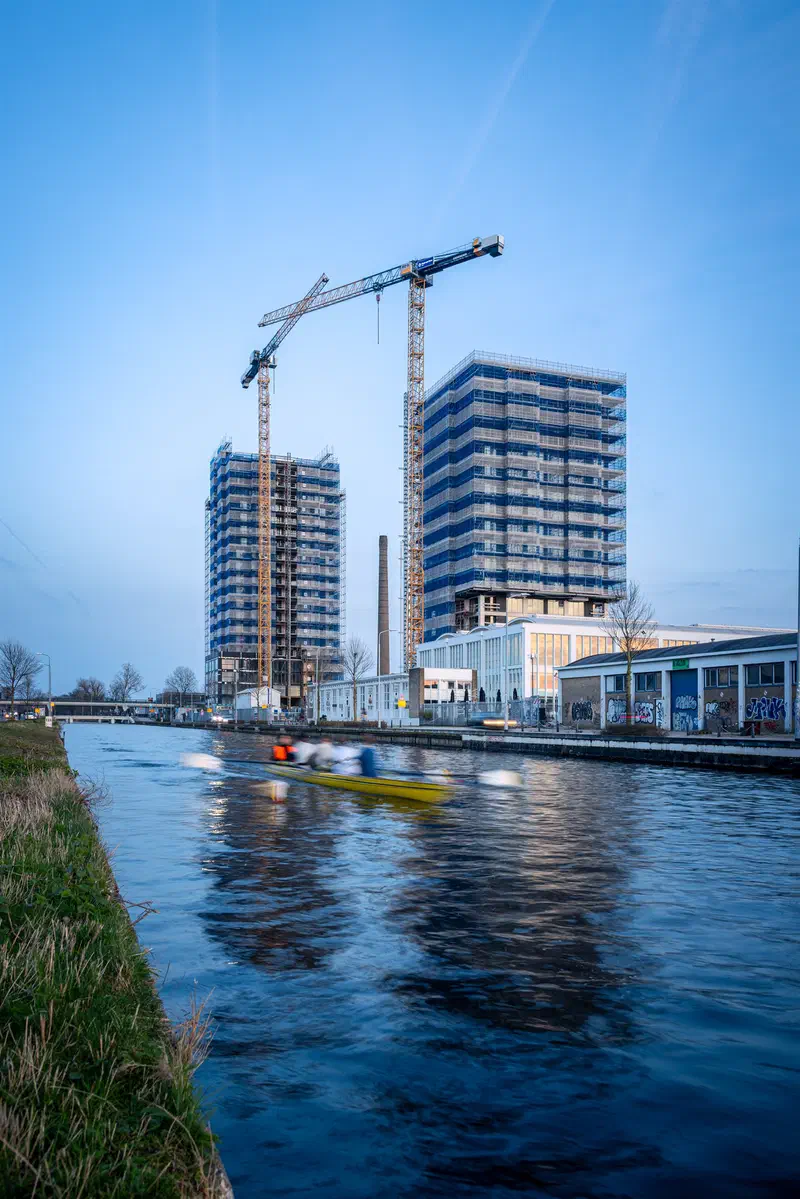 Cranes and apartment buildings (De Caai) beside a canal with a kayaker at dusk