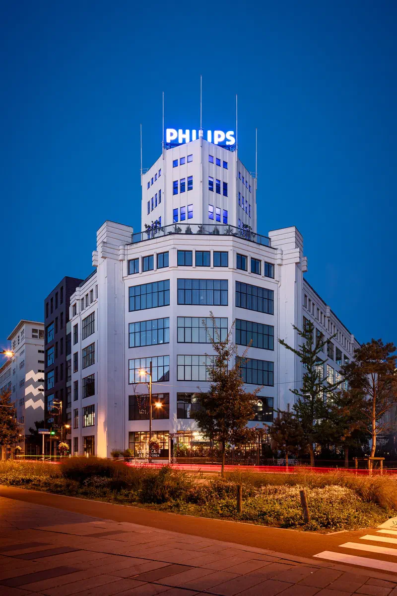 White Philips-branded building (Lichttoren) on a corner at dusk with light trails