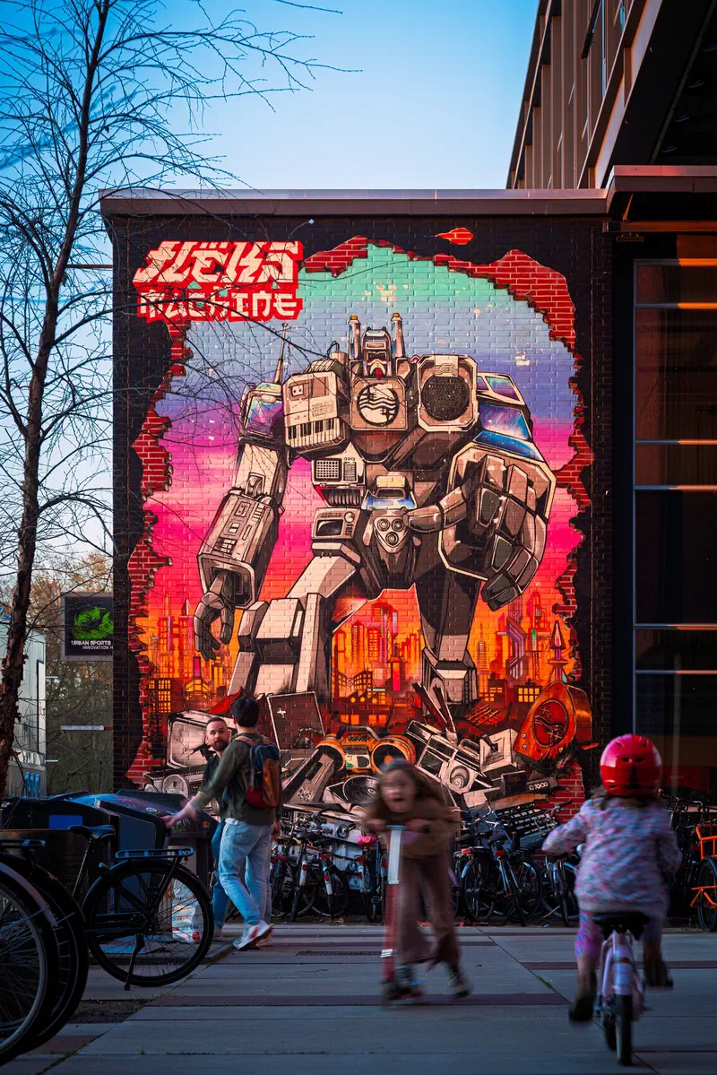 Children cycling past a large robot mural (by FLEKS) on a brick wall (Strijp-S)