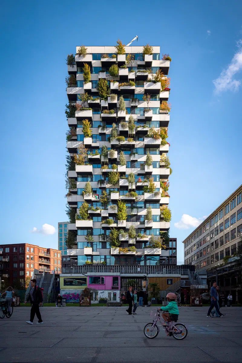 Tower covered in trees and plants (Trudo Toren) with a child on a bicycle in the square (Ketelhuisplein) below