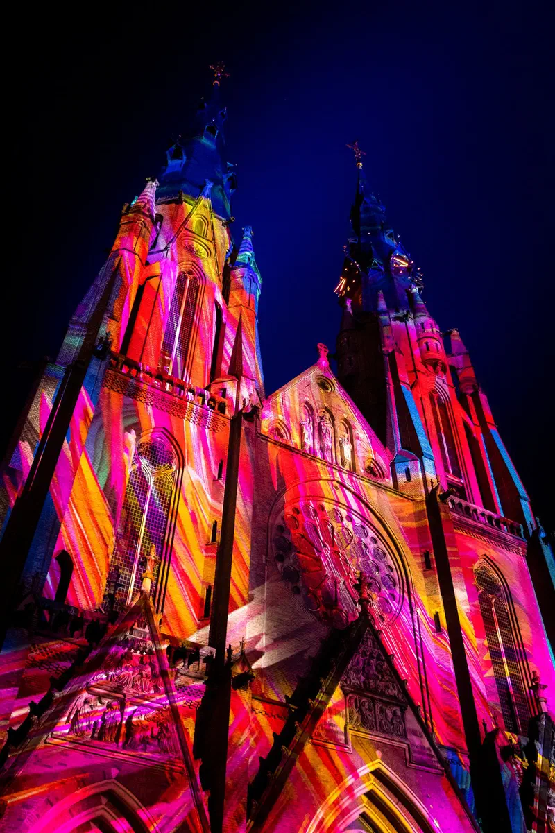Gothic church (Sint-Catharinakerk) facade covered in bright pink and orange projected light (Glow)
