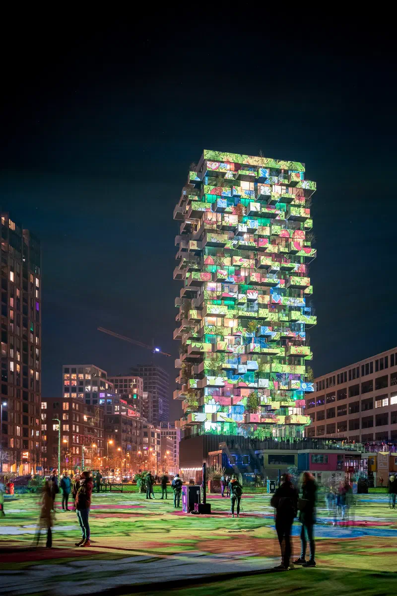 Balcony tower (Trudo Toren) covered in colourful projections above a crowd on a lit-up square (Glow)