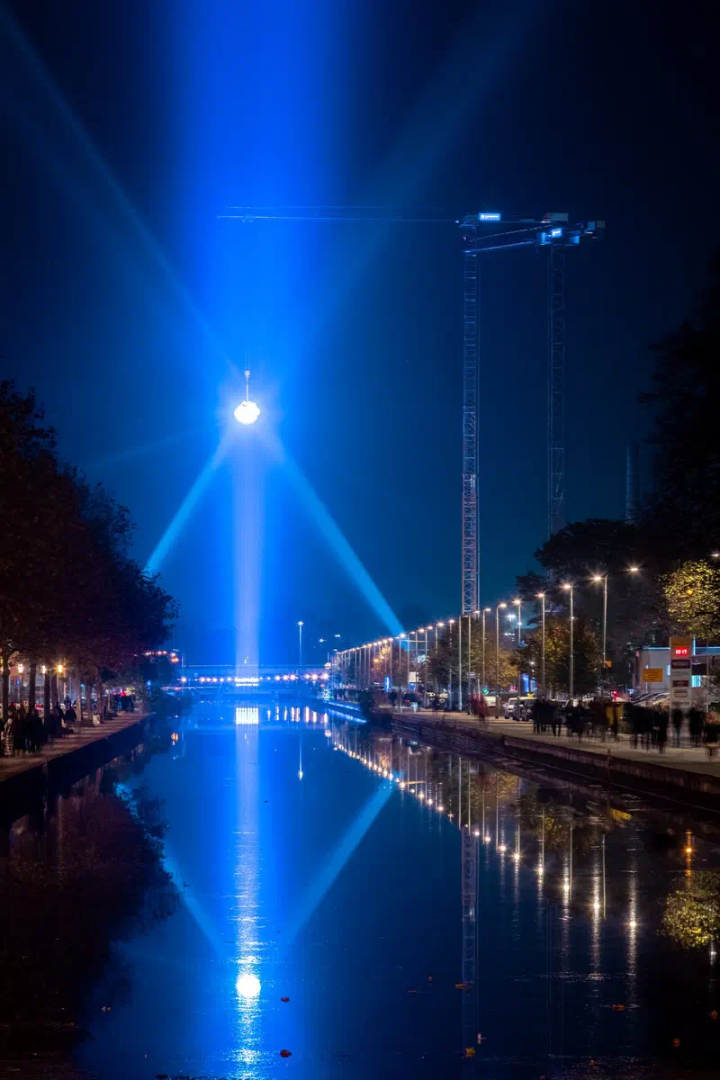 Blue light beams fanning into the sky above a canal (Glow)