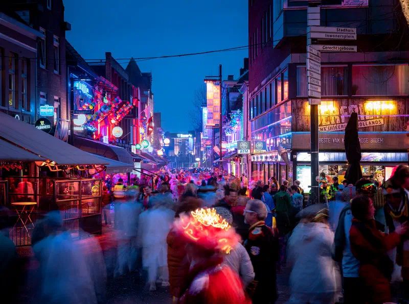 Crowded street (Stratumseind) with blurred revellers and neon signs at night during Carnaval