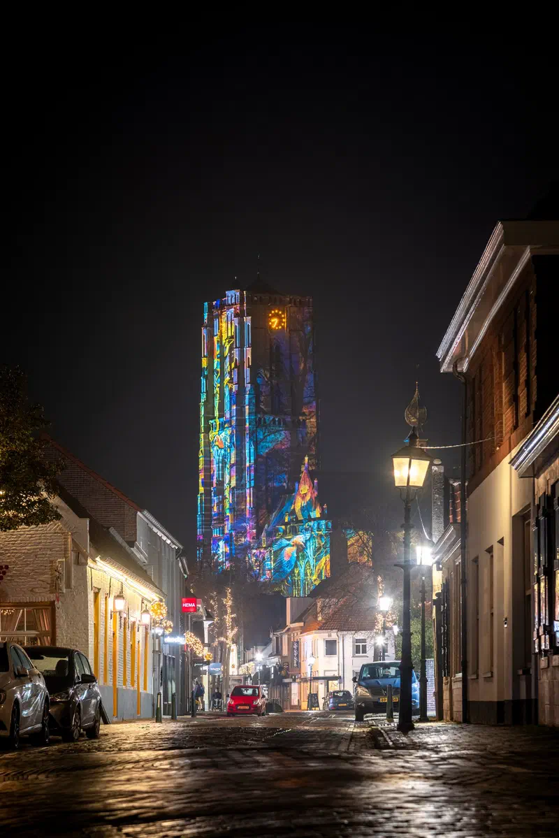 Church tower in Oirschot covered in coloured projections at the end of a quiet street (Glow)
