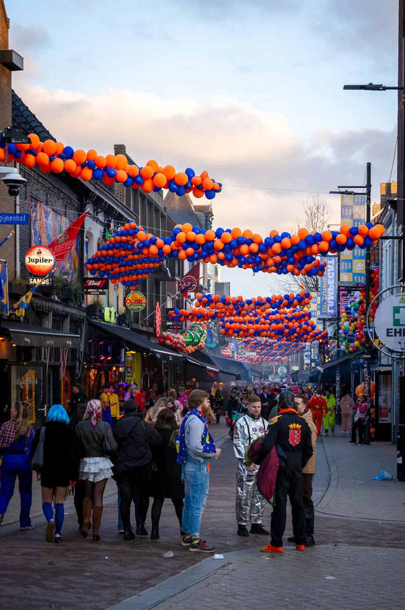 Crowd in fancy dress under orange balloon garlands on a café street (Stratumseind) during Carnaval