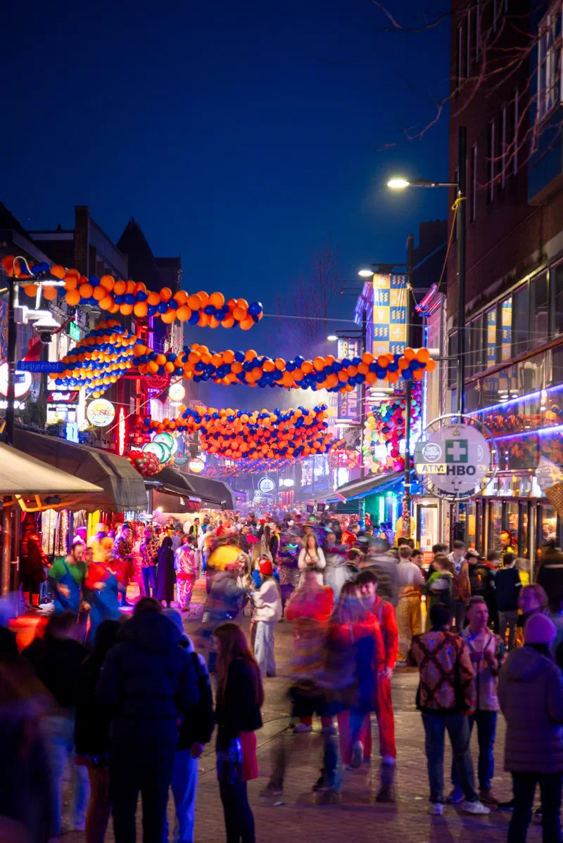 Colourful crowd in a lively street (Stratumseind) under balloon decorations at dusk during Carnaval