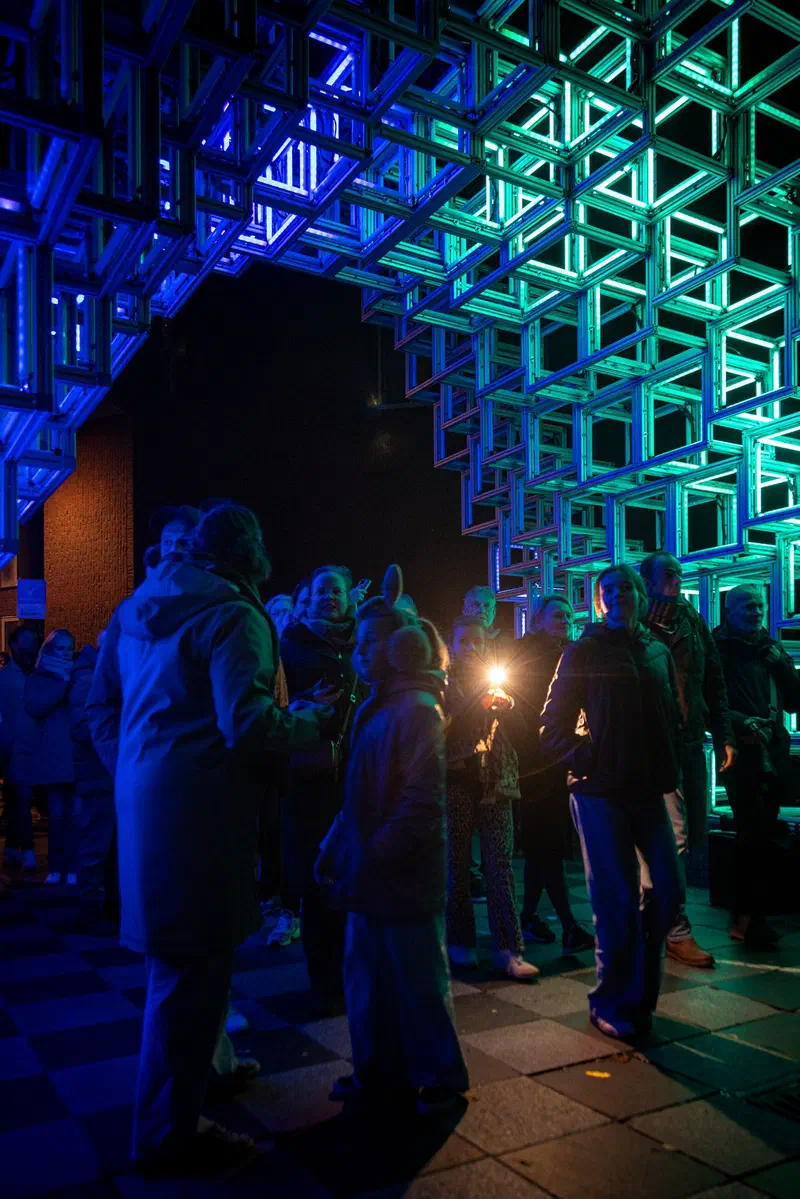 Visitors beneath a glowing blue and green lattice structure (Glow)