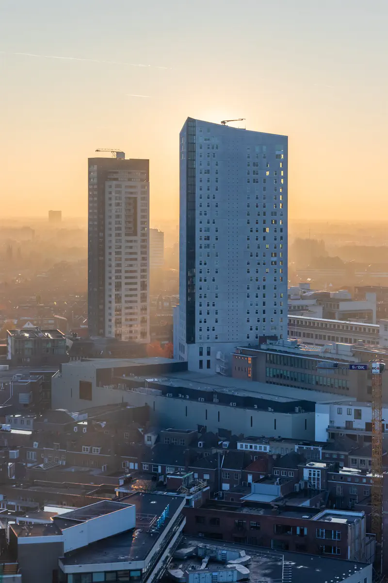 Twee hoge torens (Regent & Admirant) in warm, wazig zonsopganglicht boven de daken van Eindhoven