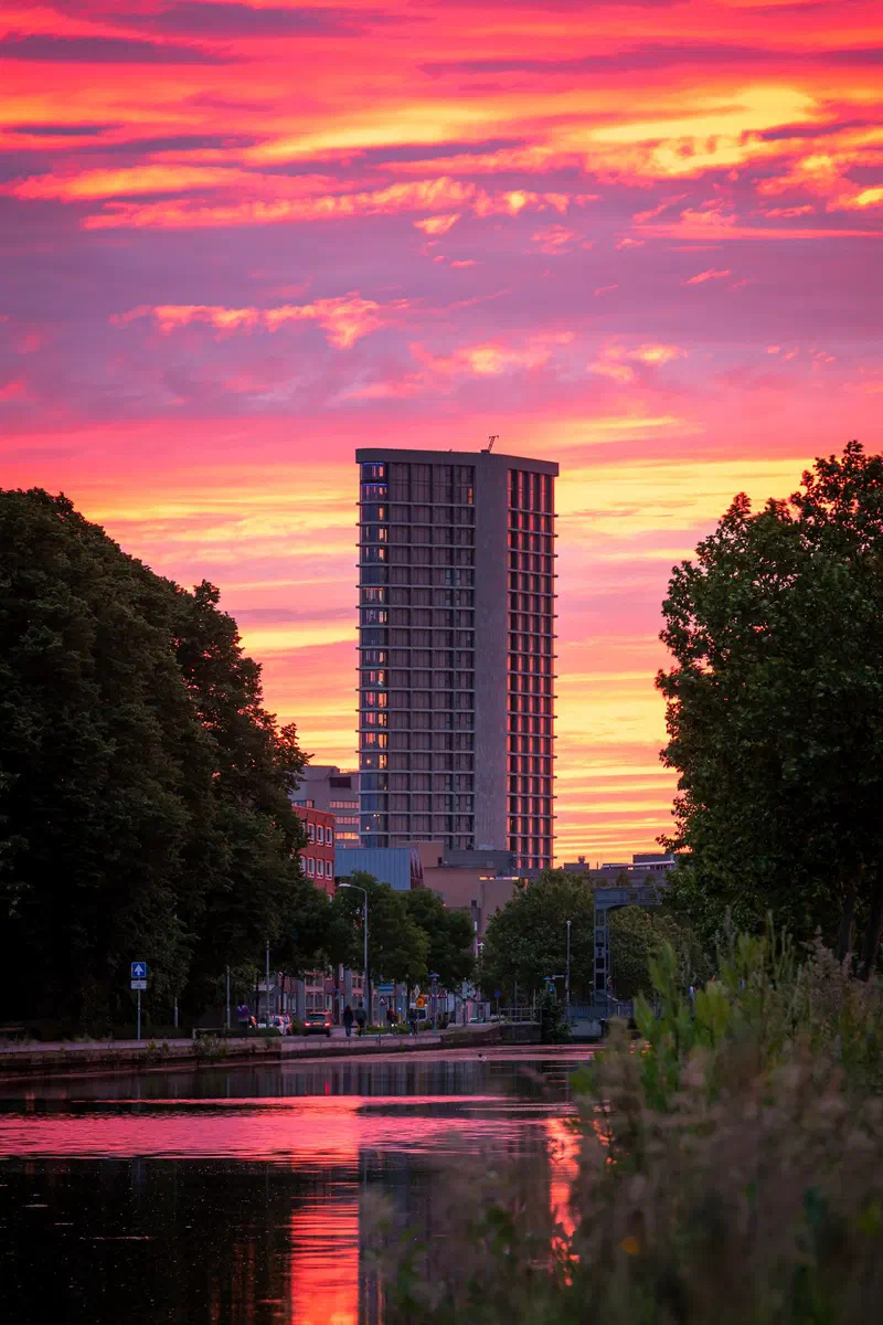 Dark apartment tower (Vestedatoren) silhouetted against a fiery sunset over a canal