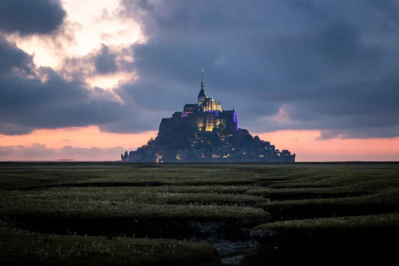 Mont-Saint-Michel silhouetted at sunset under storm clouds, France