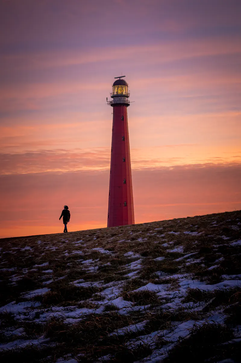 Rode vuurtoren (Lange Jaap) op een dijk met een persoon die er bij zonsondergang naartoe loopt