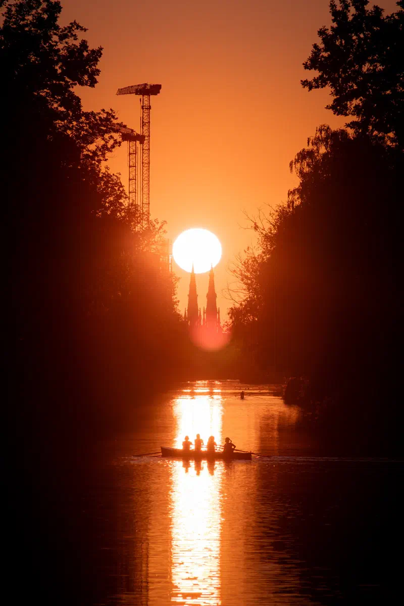 Sun setting between a church's twin spires (Sint-Catharinakerk) above a canal (Eindhovens Kanaal) with a rowing boat