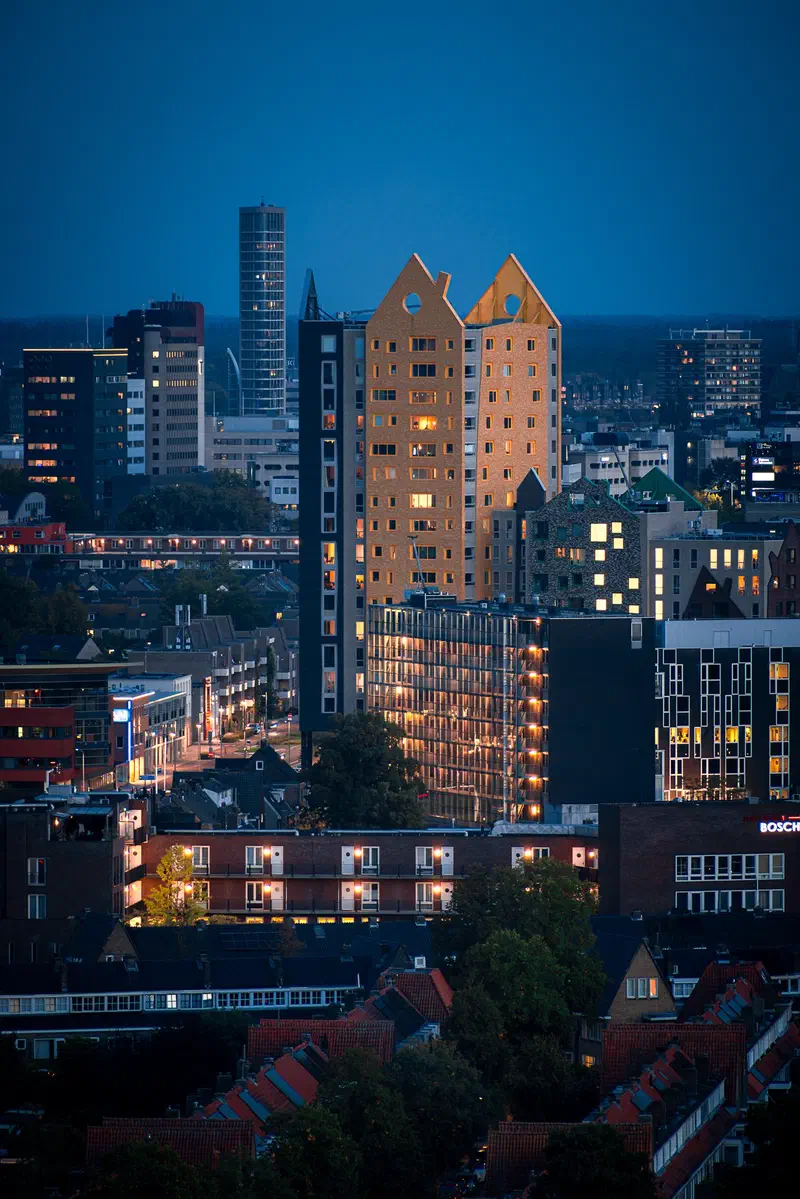 Eindhoven skyline at blue hour from the Philips Nederland building, with a gold-lit twin-gabled apartment tower