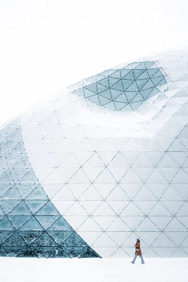 Person walking past the white glass-faceted Blob building in the snow