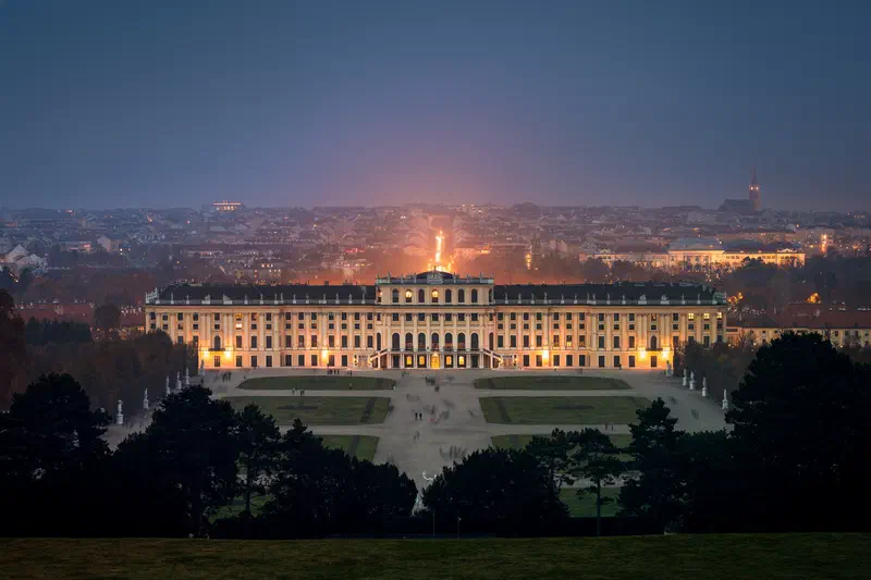 Schönbrunn Palace in Vienna lit at dusk, with formal gardens and the city beyond
