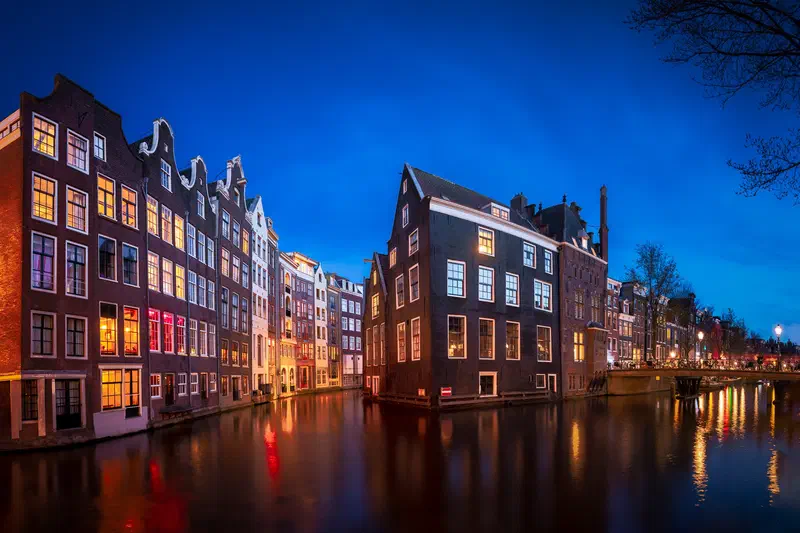 Tall canal houses reflected in the water in Amsterdam at blue hour