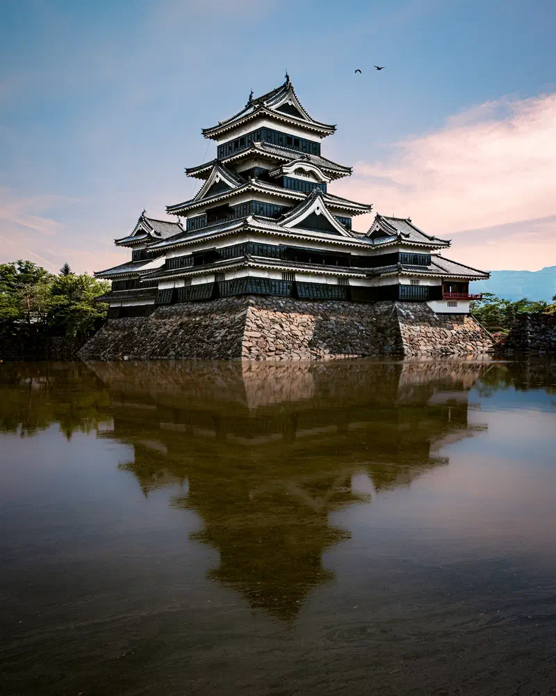 Matsumoto Castle, a black Japanese castle, reflected in calm water at sunset