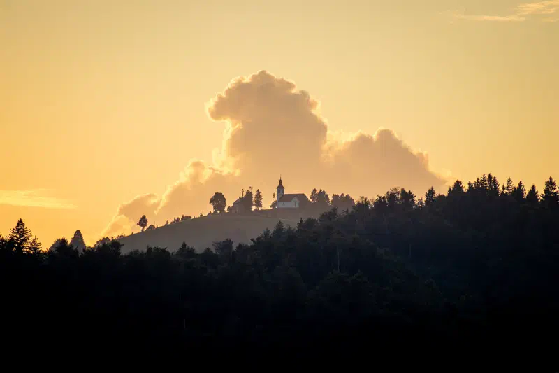 Church on a wooded hilltop beneath a glowing golden cloud, Slovenia