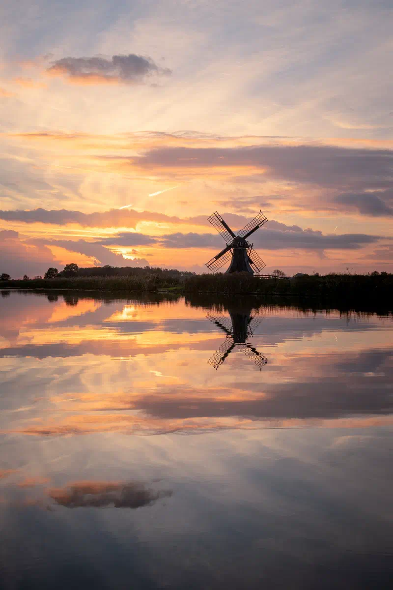 Windmill reflected in still water at sunset