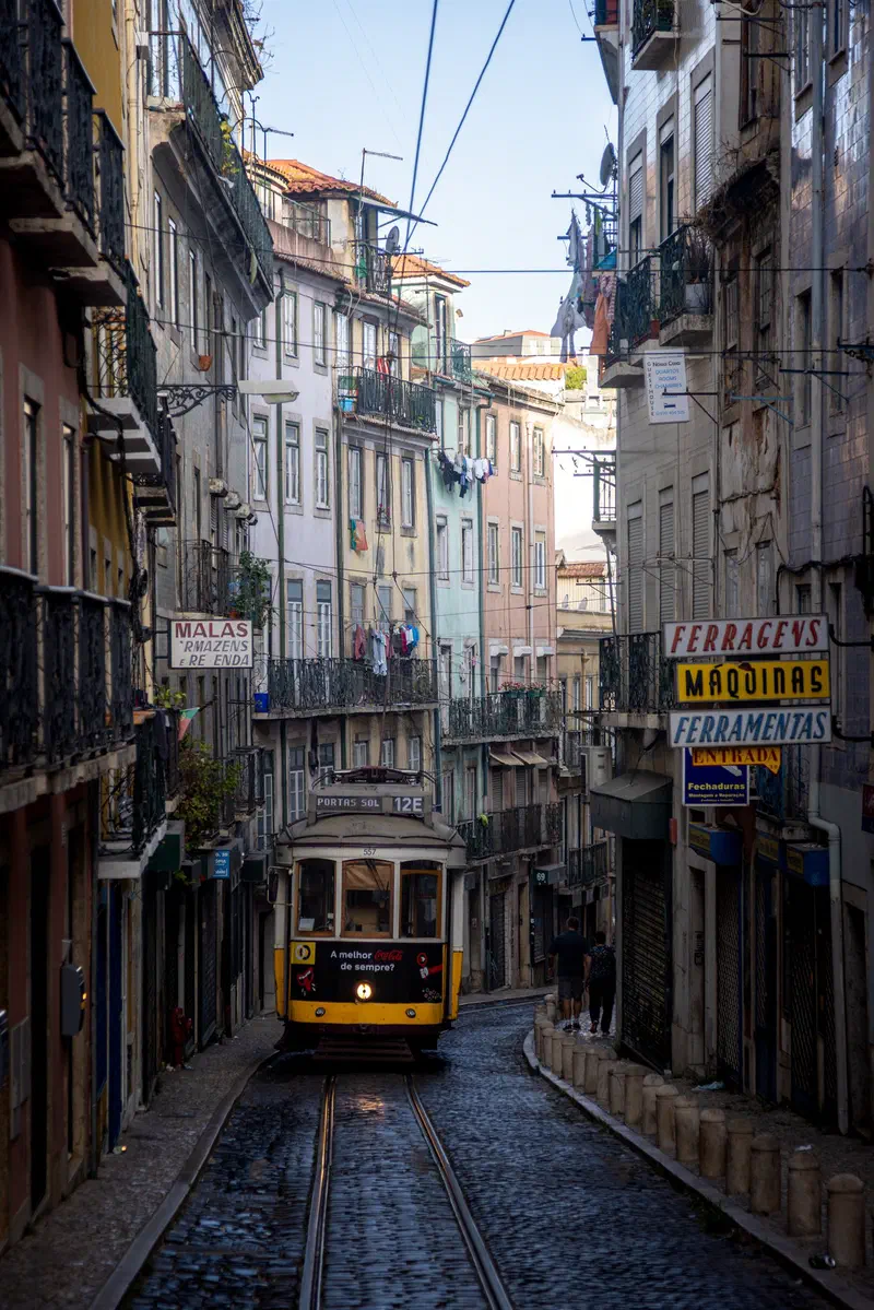 Yellow tram on a narrow cobbled street between tall old buildings in Lisbon